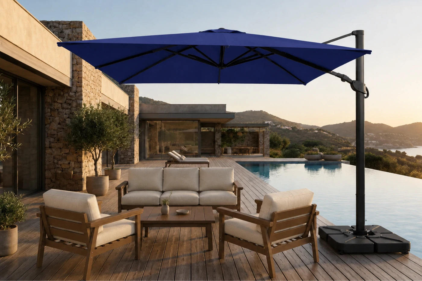 A large navy blue cantilever patio umbrella with a black pole and weighted base, shading a modern outdoor lounge set with wooden chairs and a sofa on a wooden deck beside a swimming pool.
