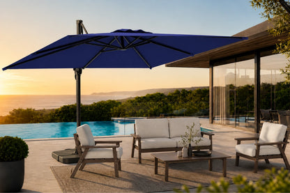 A large navy blue cantilever patio umbrella in a modern outdoor patio setting next to a swimming pool, with a wooden lounge chair, sofa, and coffee table under a warm sunset sky.