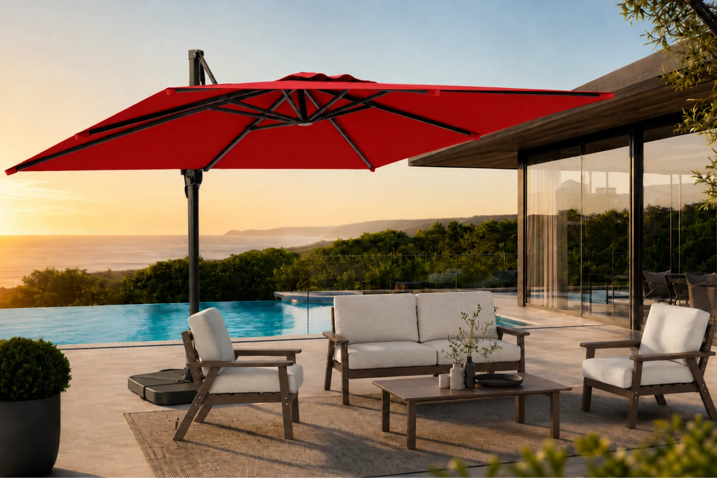 A large red cantilever patio umbrella is shown in a luxurious outdoor setting next to a swimming pool and modern patio furniture, with a sunset sky in the background.